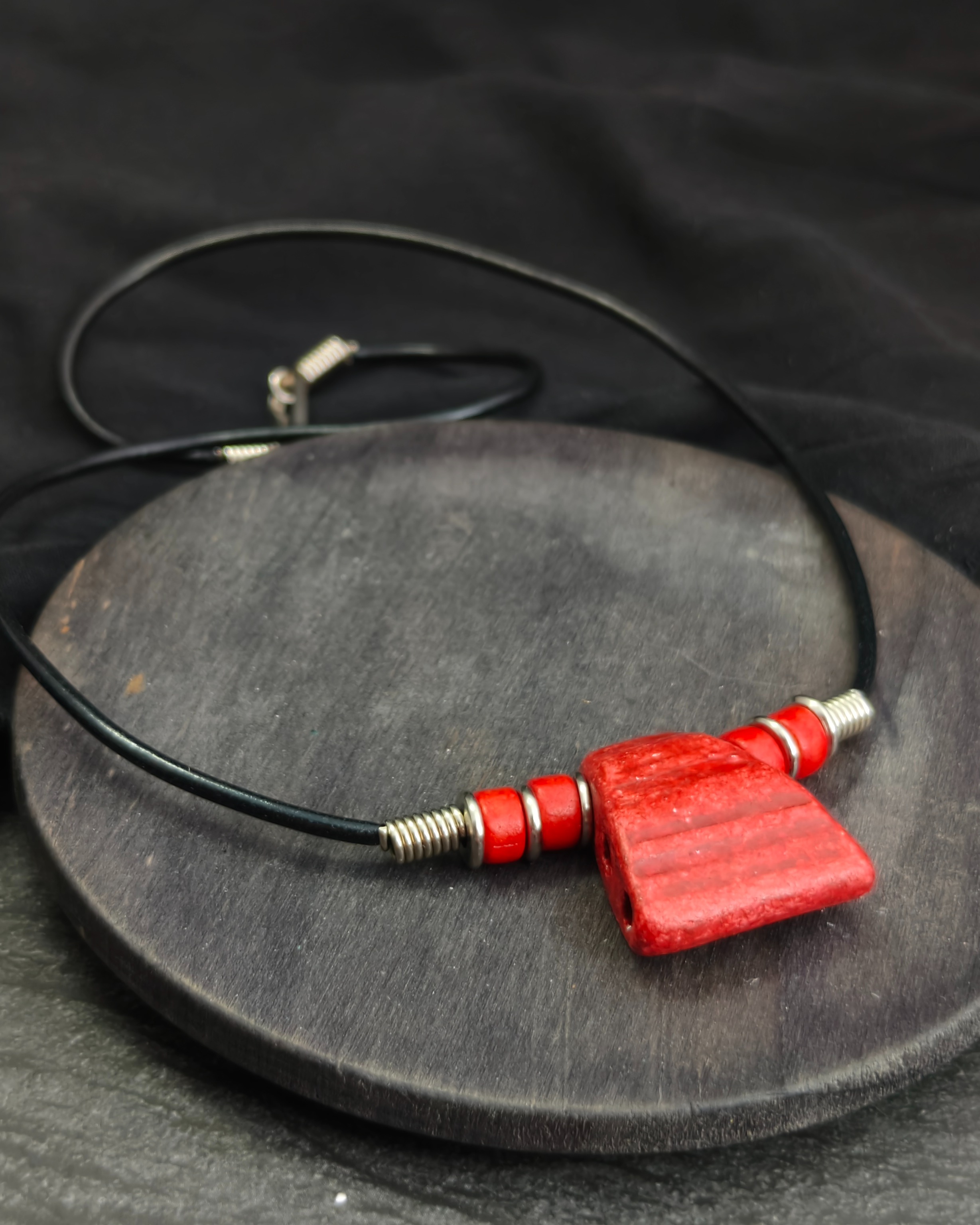 Black cord necklace with a red geometric pendant.